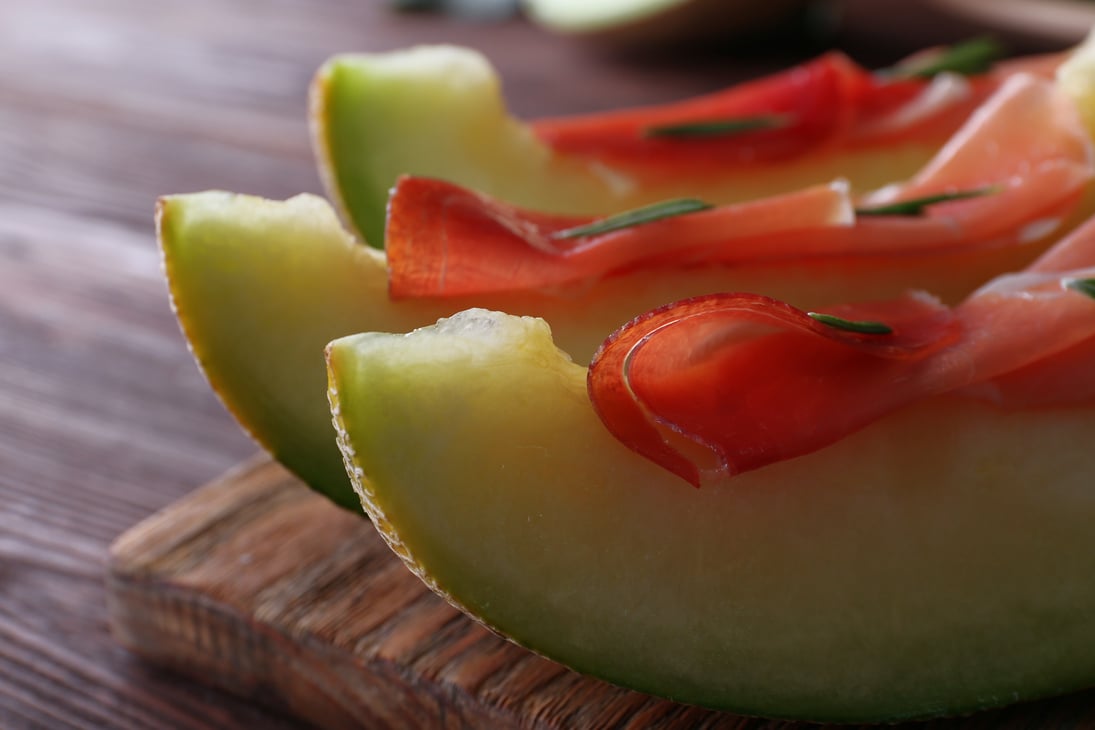 Melon with Prosciutto of Parma Ham on Wooden Table Close-up